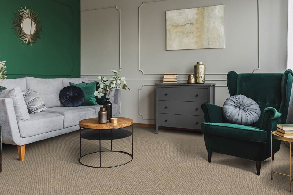 carpet in living room with grey couch and green velvet chair and mixed metal decor.